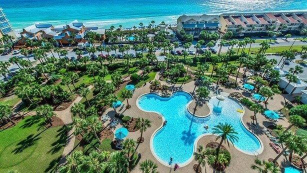 Ein Resort mit einem großen, blumenförmigen Pool, umgeben von Palmen und Liegestühlen.