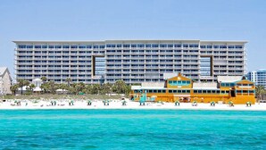 Ein großes Hotel mit mehreren Etagen und Balkonen, gelegen am Strand mit klarem, türkisblauem Wasser.