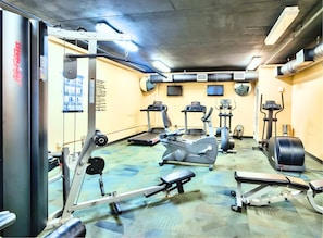 Ein Fitnessstudio mit verschiedenen Trainingsgeräten, darunter Laufbänder, Crosstrainer und Kraftgeräte.