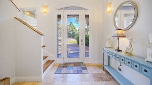 A hallway with a staircase, a door with glass panels, a console table with decorative items, and a wall-mounted mirror.