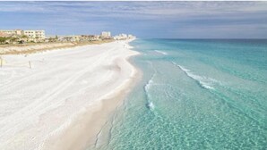 A beach with clear turquoise water, a sandy shore, and buildings in the background.