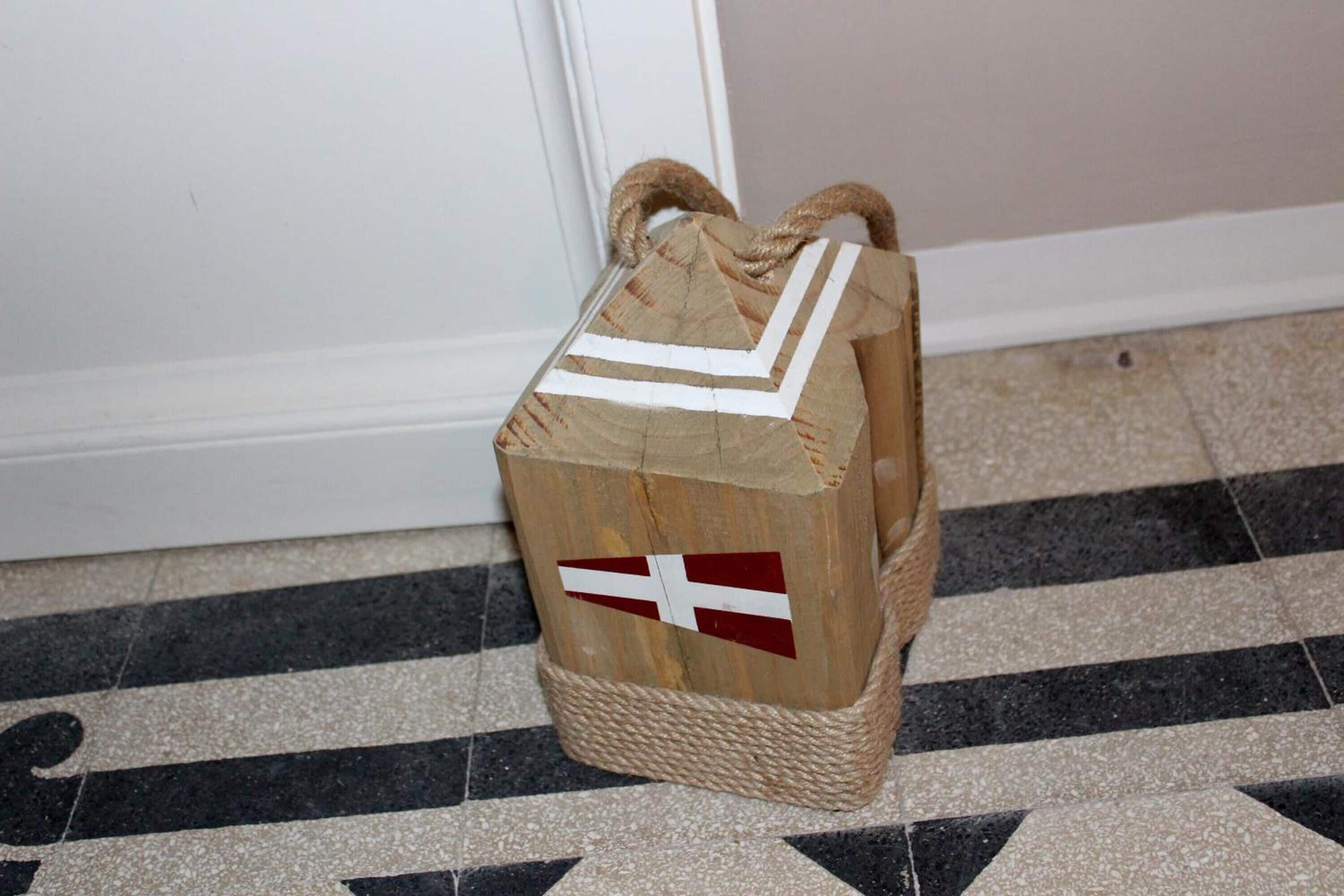 A wooden bag with a rope handle and a flag design, placed on a tiled floor.