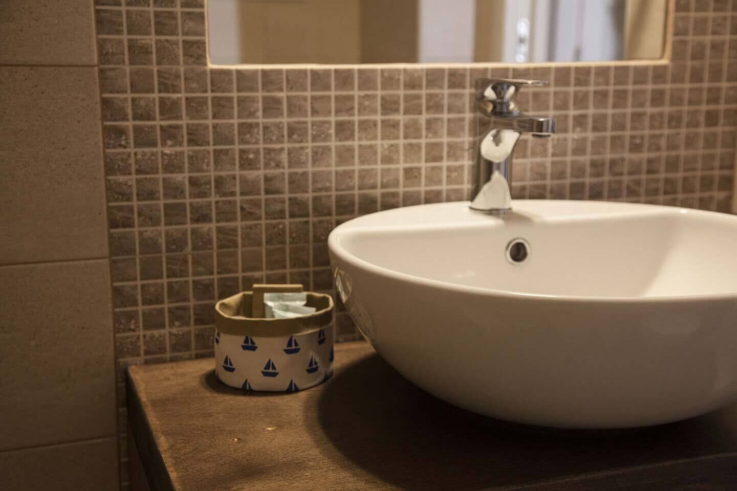 Un baño con lavamanos blanco, un espejo y un pequeño cubo de basura con diseños de veleros.