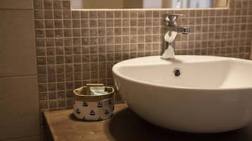 Un baño con lavamanos blanco, un espejo y un pequeño cubo de basura con diseños de veleros.