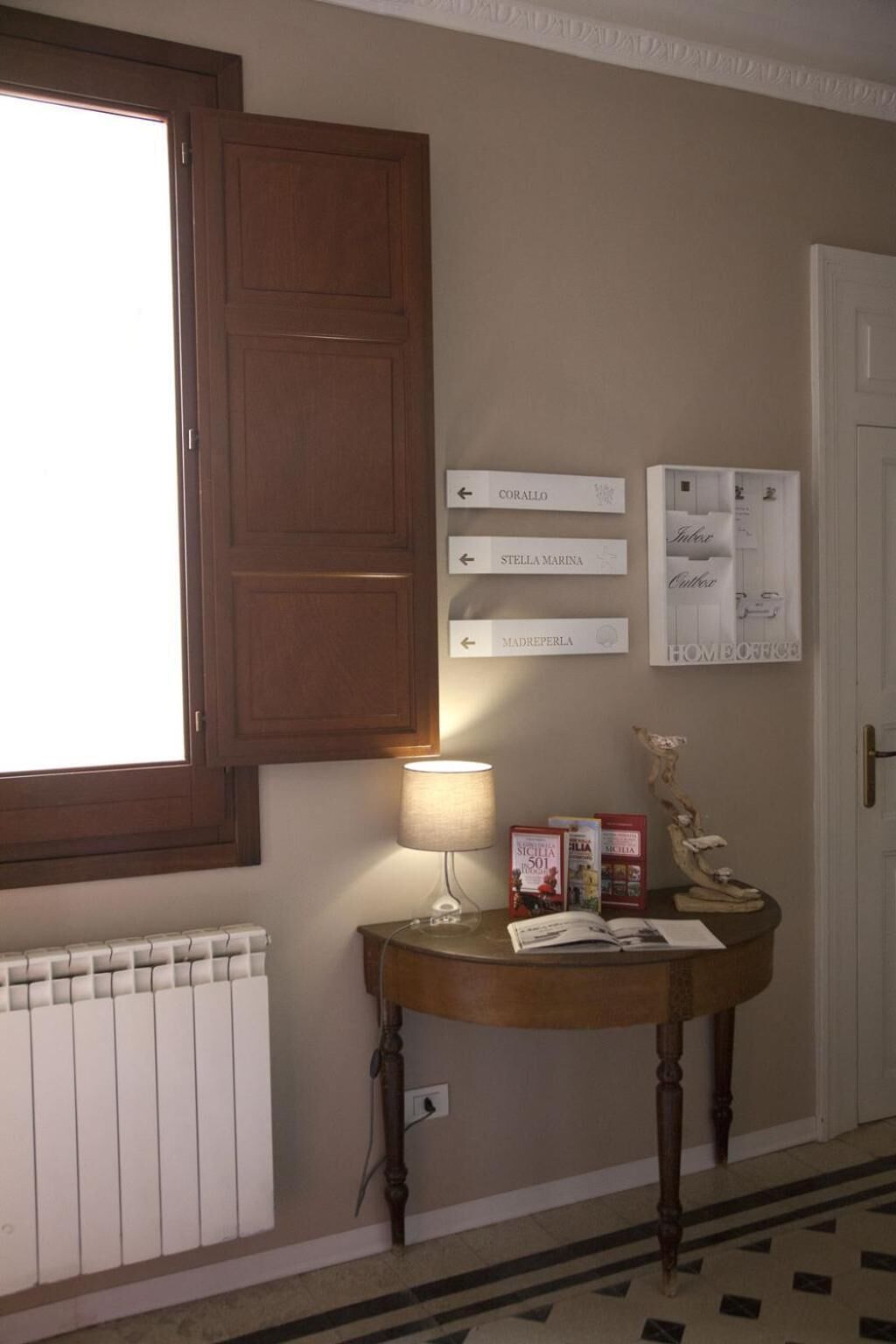 Une pièce avec un meuble en bois, une table avec une lampe, des livres et un radiateur. Des panneaux indicateurs sont accrochés au mur.