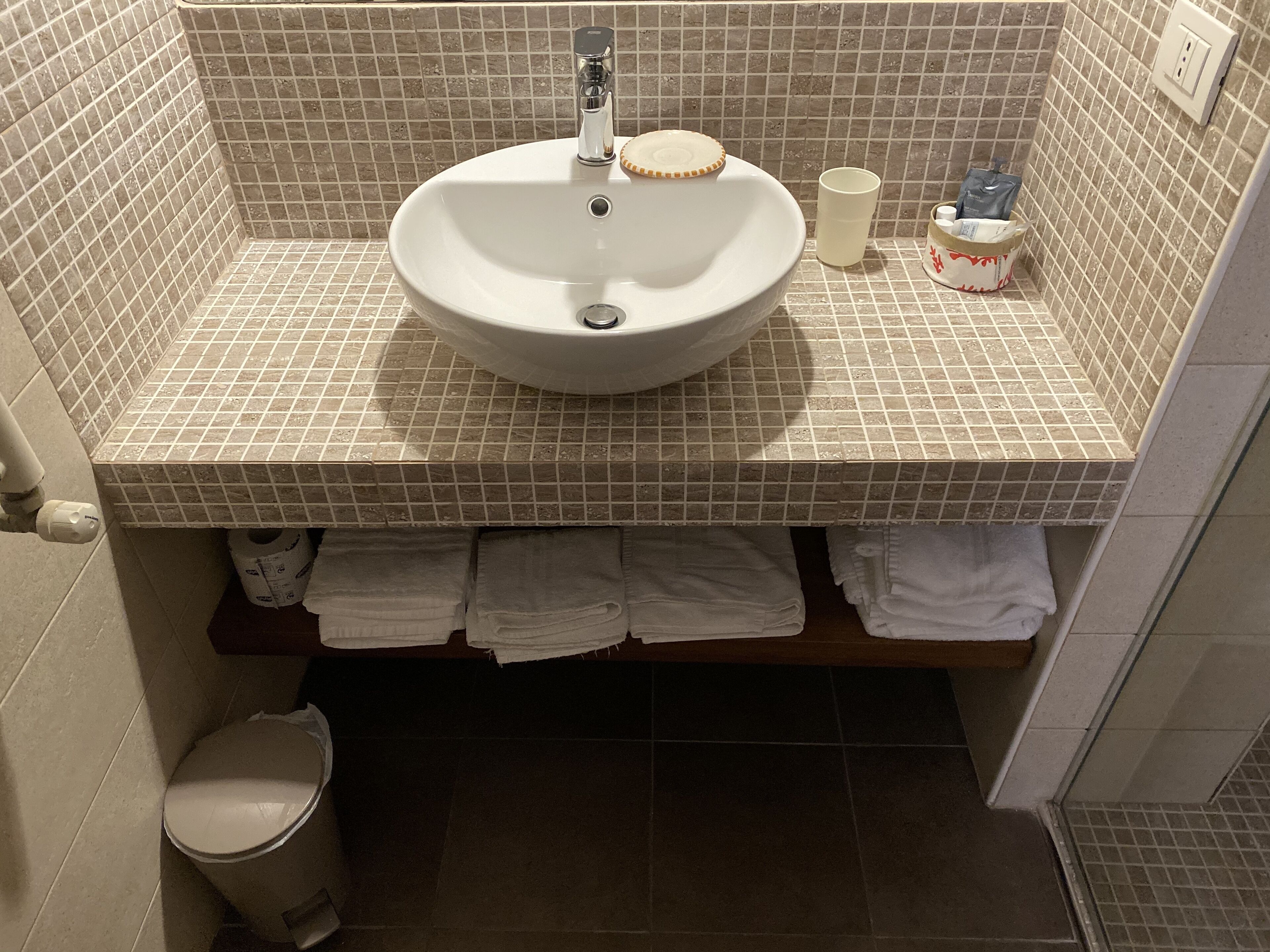 Ein Badezimmer mit einem weißen Waschbecken, einer Toilette und einem Regal mit Handtüchern.
