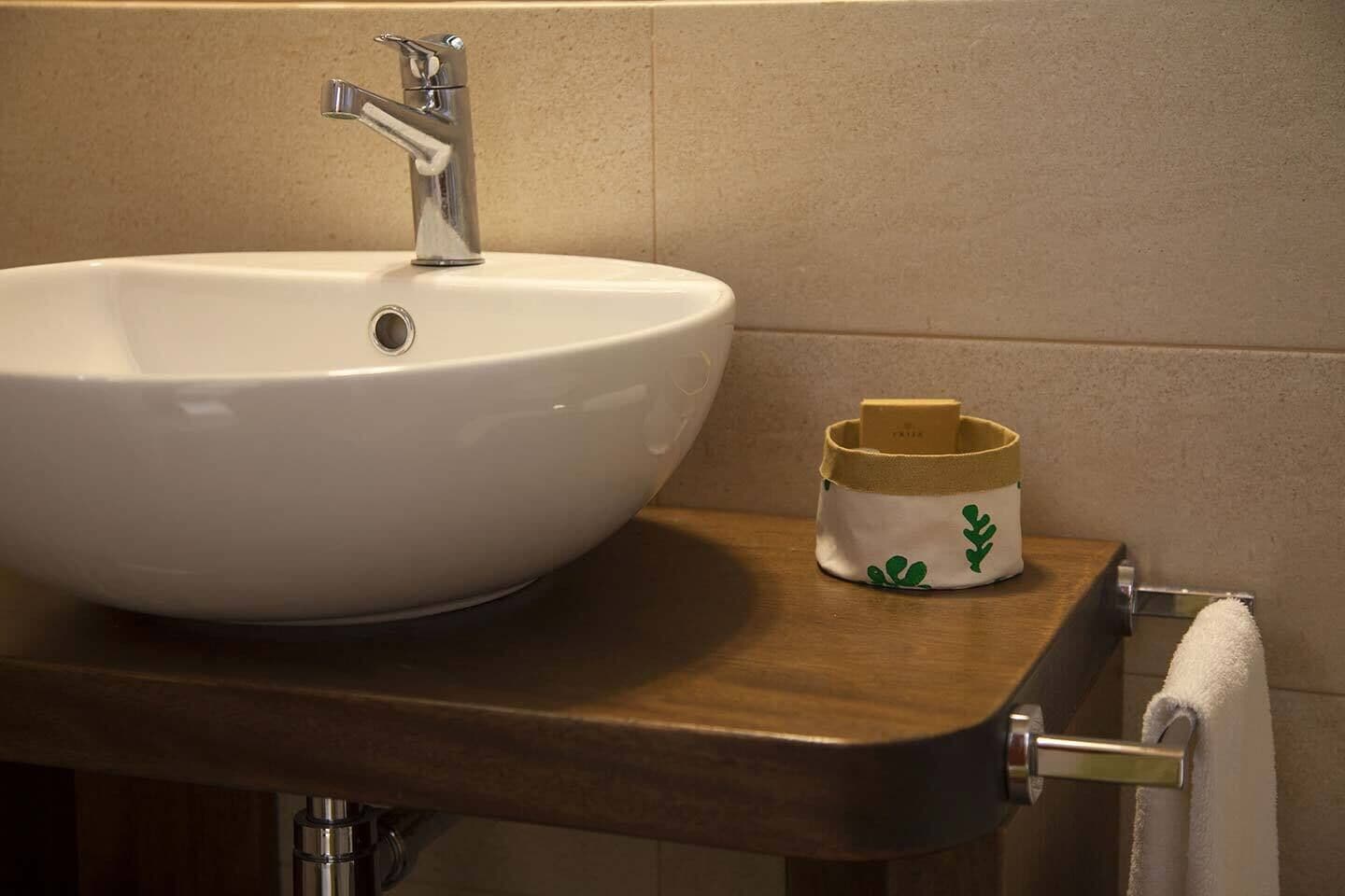 Ein Badezimmer mit einem weißen Waschbecken, einer Holzablage und einem kleinen Behälter mit einem Design aus grünen Blättern.