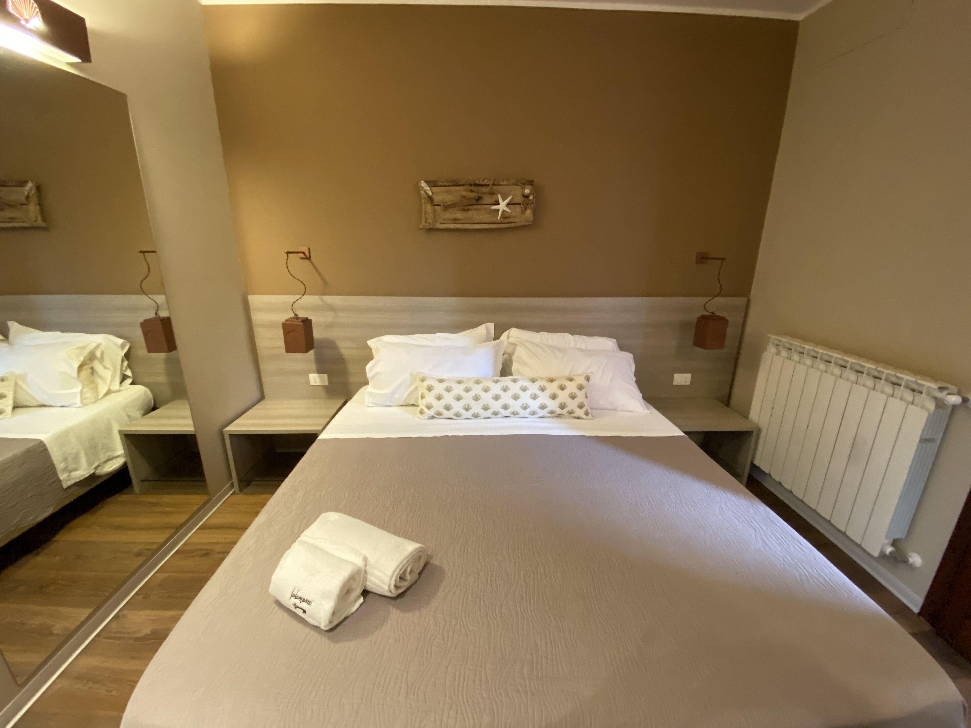 Ein Hotelzimmer mit einem großen Bett, zwei Nachttischen, einem Holz-Kopfteil und einer Wandleuchte.