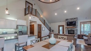 A spacious living area with a dining table, kitchen, and a staircase leading to an upper level. - Hot Tub • Game Loft • Walk to Local Attractions • Sleeps 10 (Broken Bow)