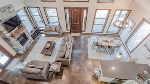 A spacious living area with a stone fireplace, a large sofa set, and a dining table. - Hot Tub • Game Loft • Walk to Local Attractions • Sleeps 10 (Broken Bow)