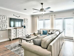 A living room with a sectional sofa, a flat-screen TV, a ceiling fan, and decorative wall art. - Luxury Townhome, Golf Cart, Short Walk to Beach, Pool, Sleeps 13 (Miramar Beach)
