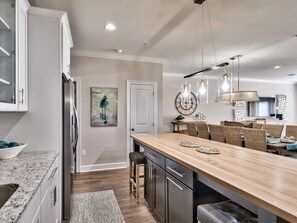 A modern kitchen with a wooden island, stainless steel appliances, and a dining area with wicker chairs. - Luxury Townhome, Golf Cart, Short Walk to Beach, Pool, Sleeps 13 (Miramar Beach)