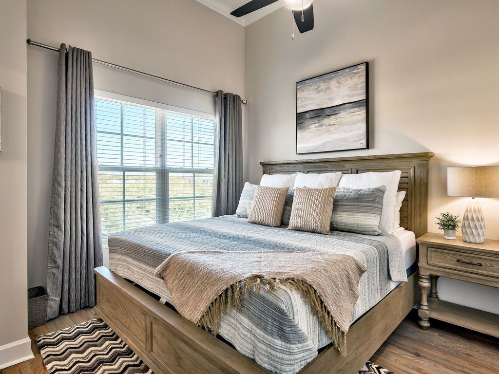 Ein Schlafzimmer mit einem großen Bett, einem Nachttisch, einem Fenster mit Vorhängen und einem Deckenventilator.