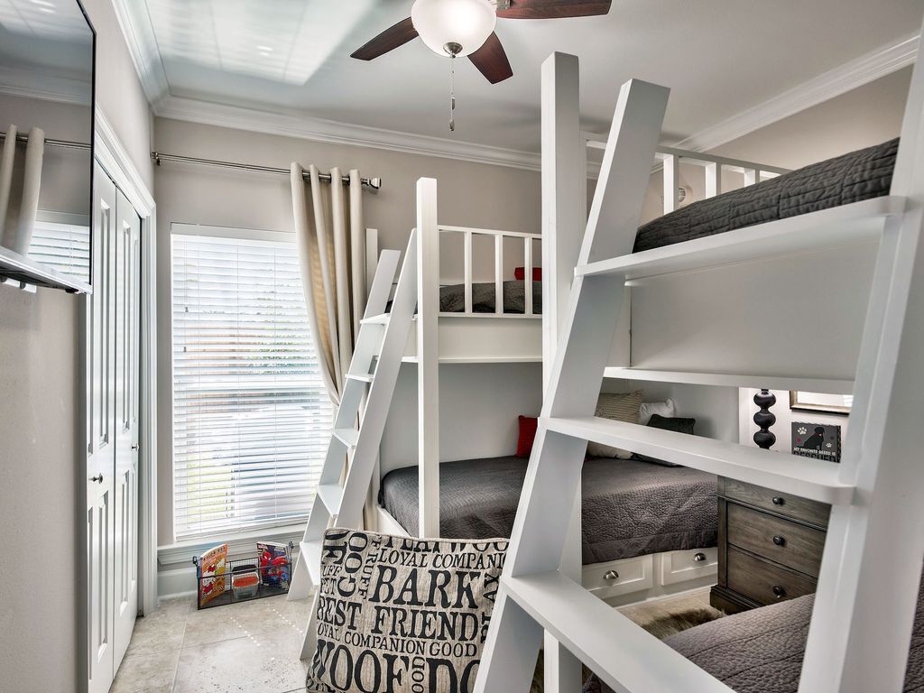 Quarto com beliches, ventilador de teto, janela com persianas e porta.