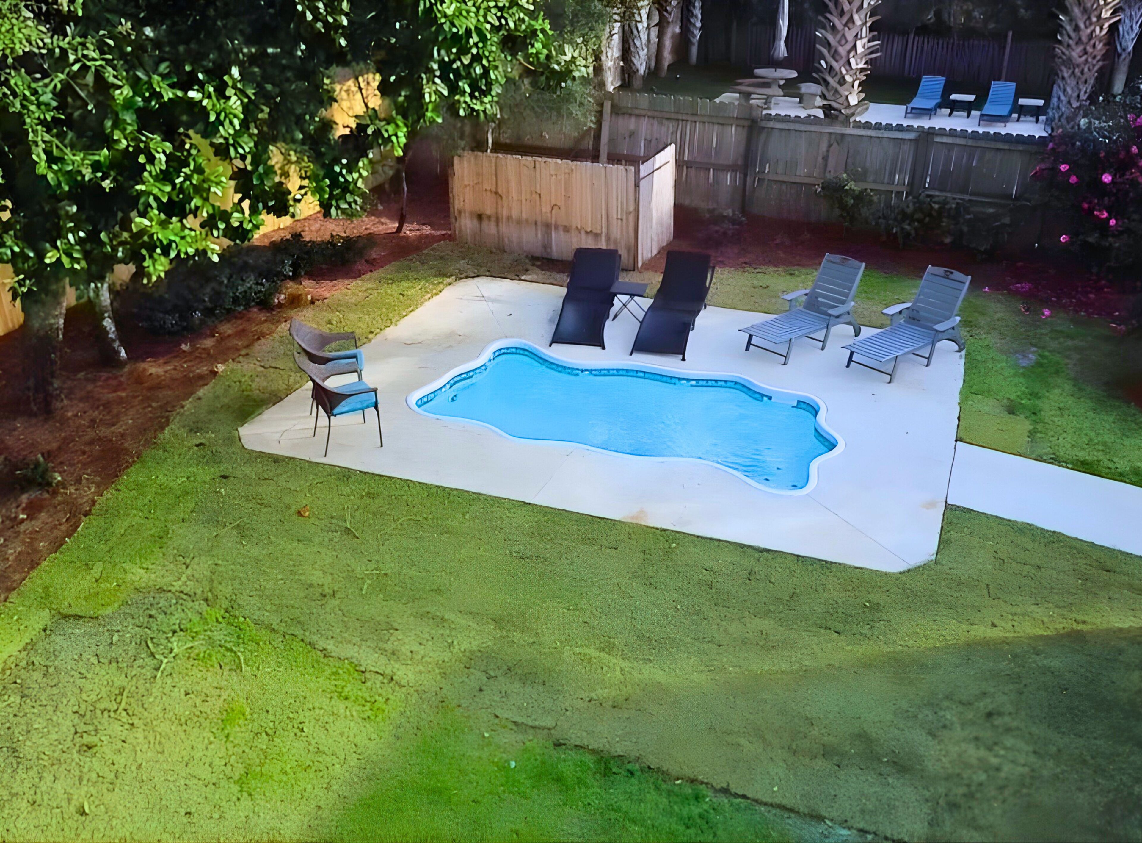 Ein Garten mit Swimmingpool, umgeben von einer Holzterrasse, ausgestattet mit Liegestühlen und einem kleinen Tisch.