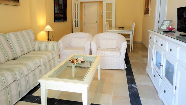 Un salon comprenant un canapé, deux fauteuils, une table basse et un téléviseur posé sur un meuble.