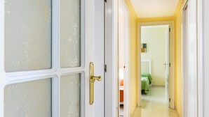 Un couloir avec une porte blanche dotée de panneaux en verre dépoli et d’une poignée en laiton, qui mène à une pièce contenant un lit et une couverture verte.