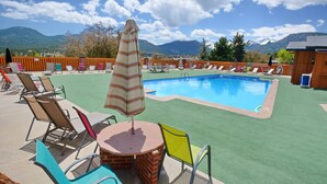 A swimming pool with lounge chairs and a table, surrounded by a wooden fence, with mountains in the background. - Charming 2 Bedroom w/ Private Hot Tub and Mountain views! (Estes Park)