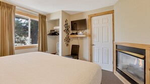 A bedroom with a large bed, a fireplace, a TV mounted on the wall, and a closet with a mirror. - Charming 2 Bedroom w/ Private Hot Tub and Mountain views! (Estes Park)