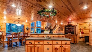 A cozy cabin interior with a wooden dining area, a kitchen with a central island, and a bar area.