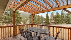 Una terraza techada al aire libre con una pérgola de madera, una mesa redonda y sillas de metal.