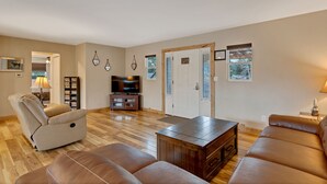 Amplia sala de estar con un sofá beige, un sillón reclinable, una mesa de centro de madera y un televisor.