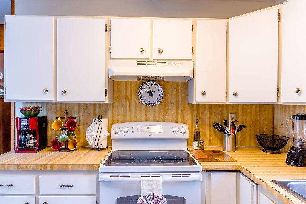 Una cocina con armarios blancos, una estufa, un reloj y diversos electrodomésticos.