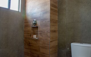 A bathroom with a wooden vanity, a toilet, and a shelf with toiletries.