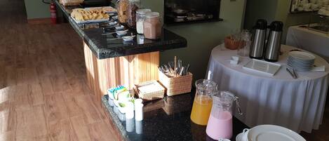 A breakfast buffet setup with various food items, beverages, and utensils on a counter and tables.