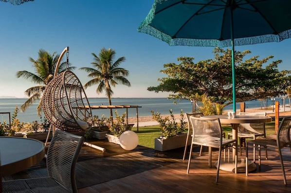 A beachside patio with wicker furniture, a round table, and a large umbrella. - Pousada Algodão da Praia (Araruama)