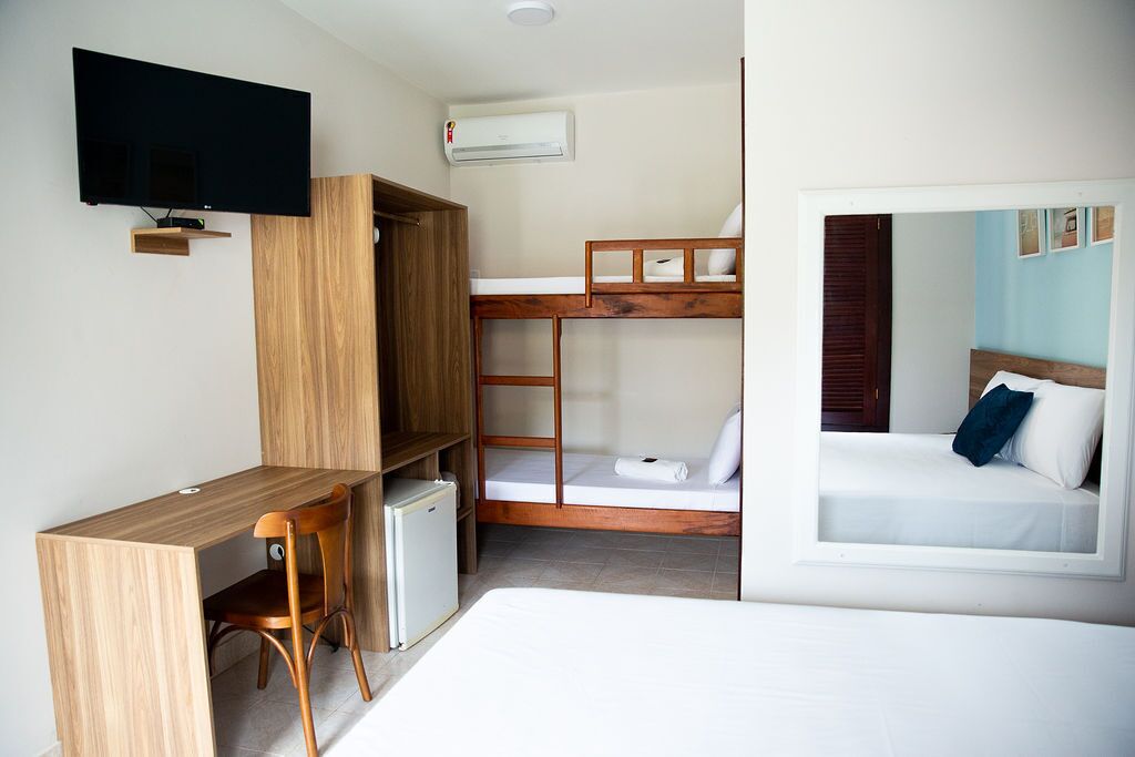 A compact room with bunk beds, a desk, a chair, a TV, and an air conditioning unit.