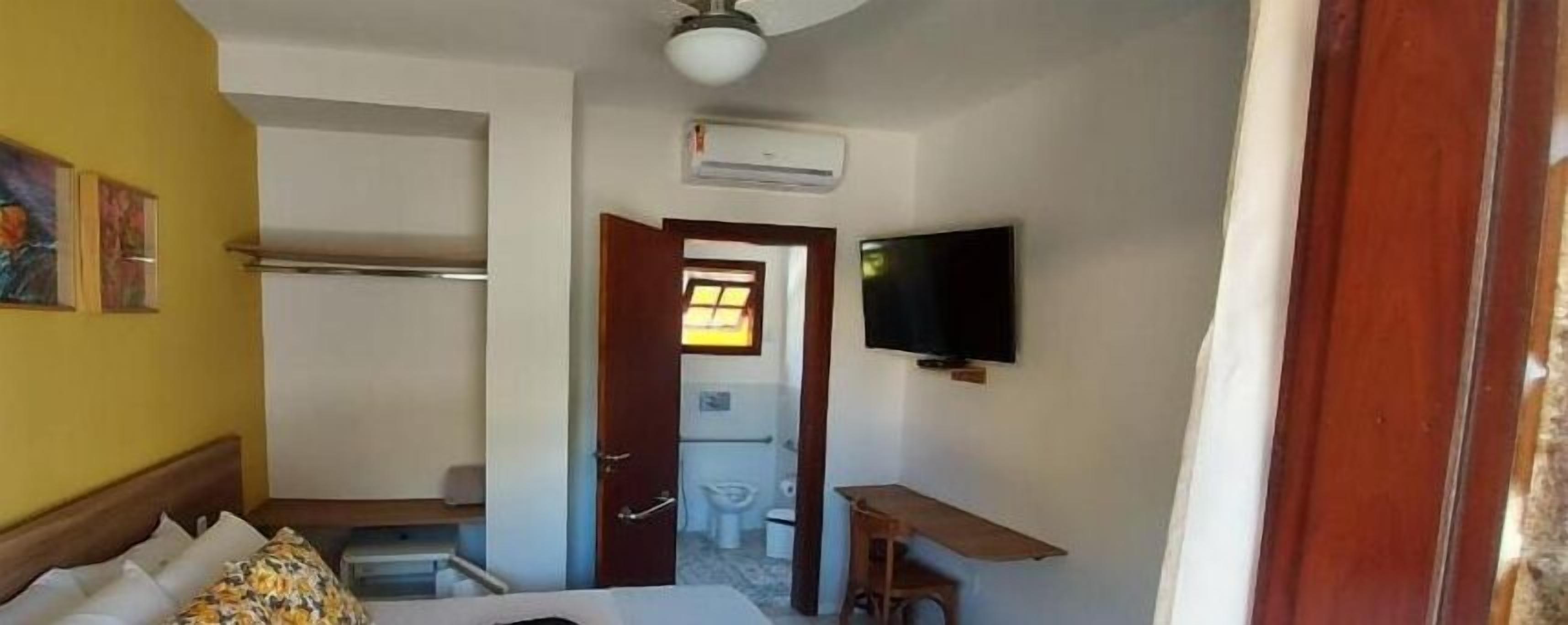 A hotel room with a bed, a TV mounted on the wall, an air conditioning unit, and a door leading to a bathroom.