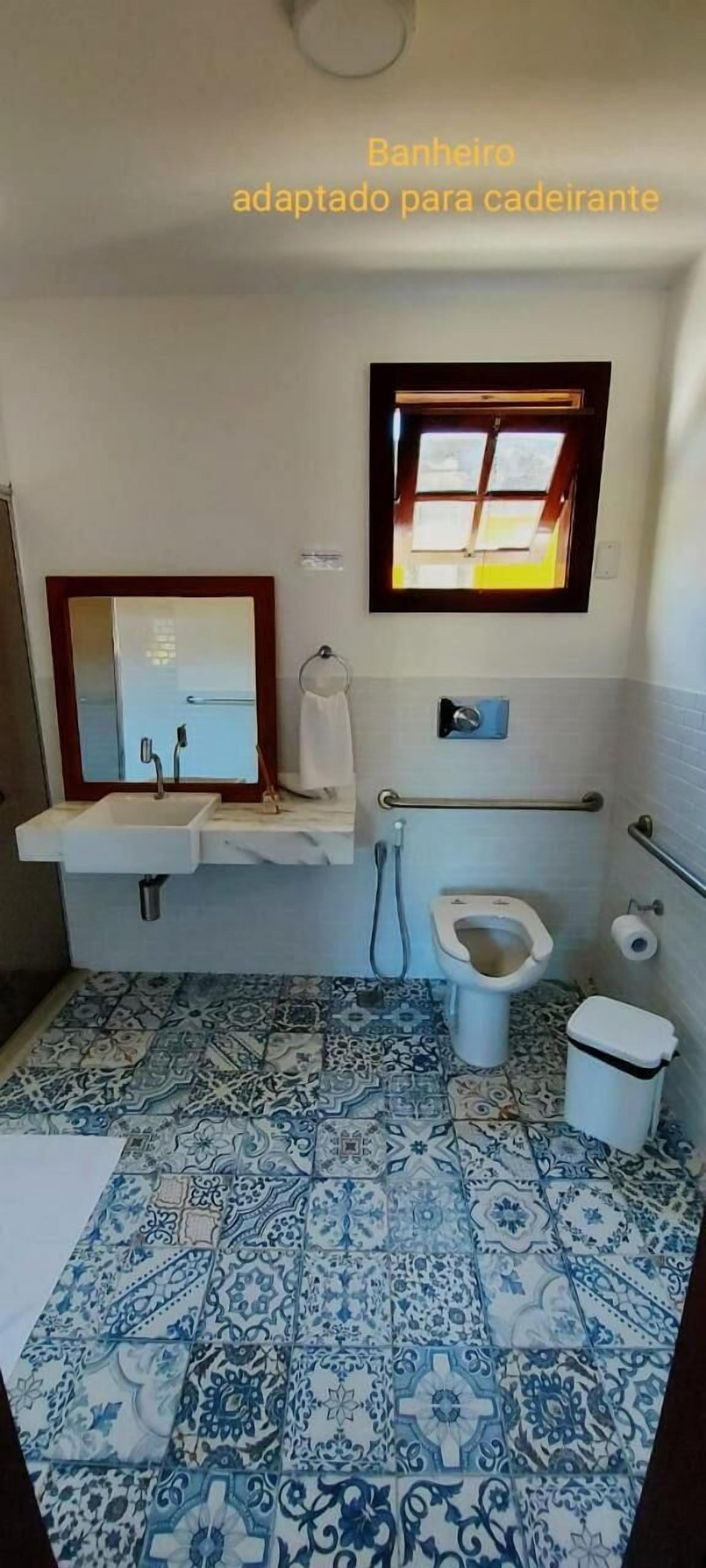 A bathroom with a sink, mirror, toilet, and window.
