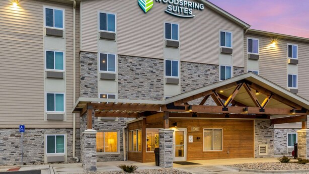 A multi-story hotel with a stone facade, a covered entrance, and a sign reading "Woodspring Suites". - WoodSpring Suites Indianapolis Castleton (Indianapolis)