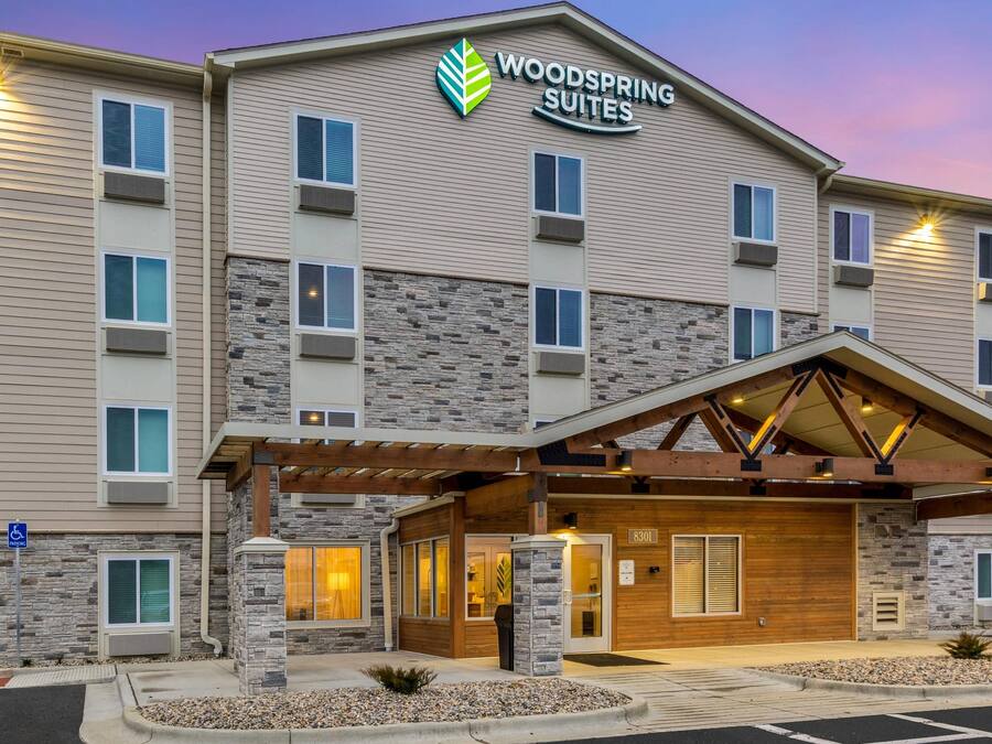 A multi-story hotel with a stone facade, a covered entrance, and a sign reading 'Woodspring Suites.'