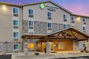 Un hotel de varios pisos con fachada de piedra, un acceso cubierto y un letrero que dice 'Woodspring Suites'.