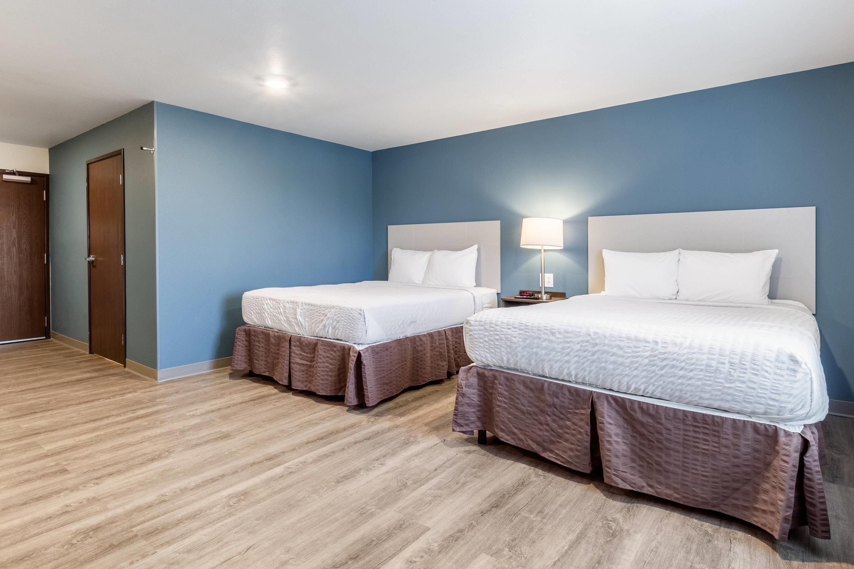 A hotel room with two beds, a wooden floor, and a blue wall.