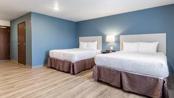 A hotel room with two beds, a wooden floor, and a blue wall.
