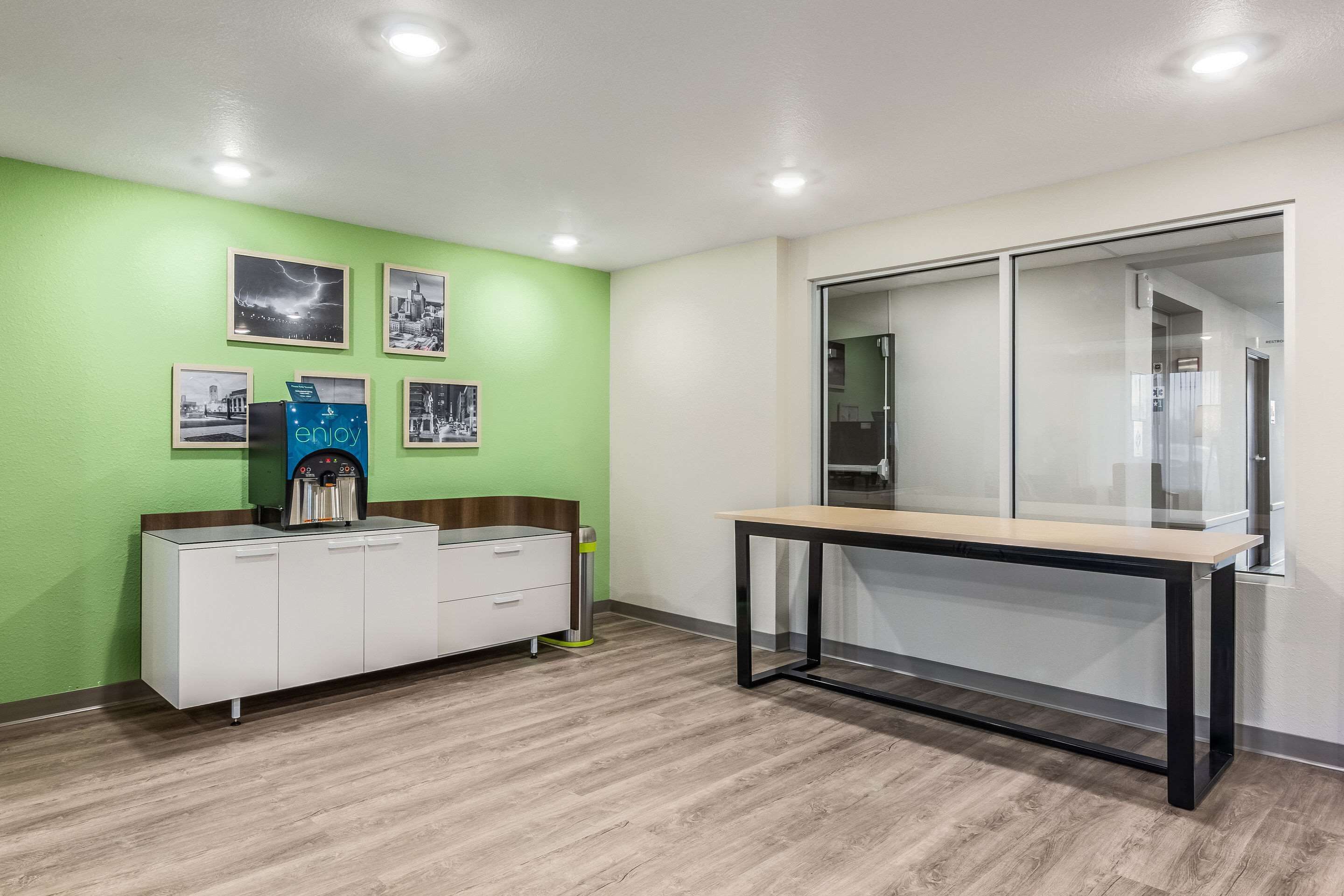 A modern office space with a green wall, a white cabinet with drawers, a water dispenser, and a glass-walled desk area.