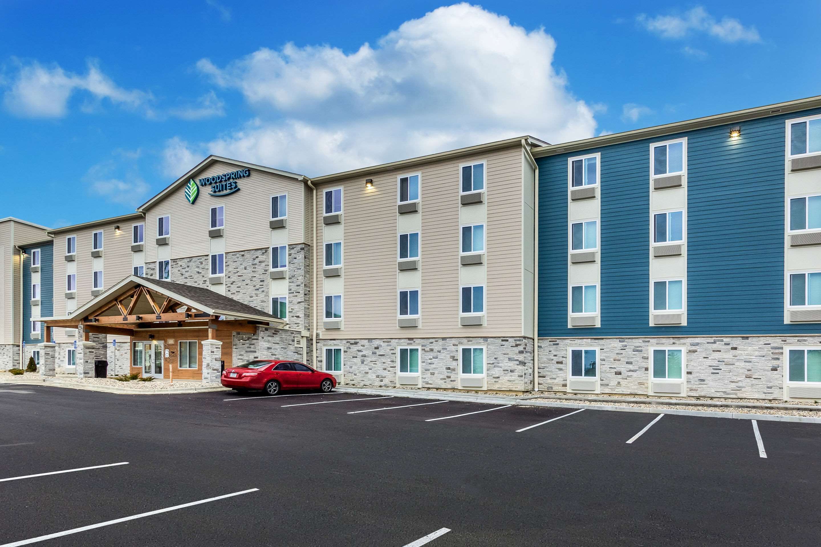 A multi-story hotel with a stone facade, a red car parked in front, and a clear blue sky.