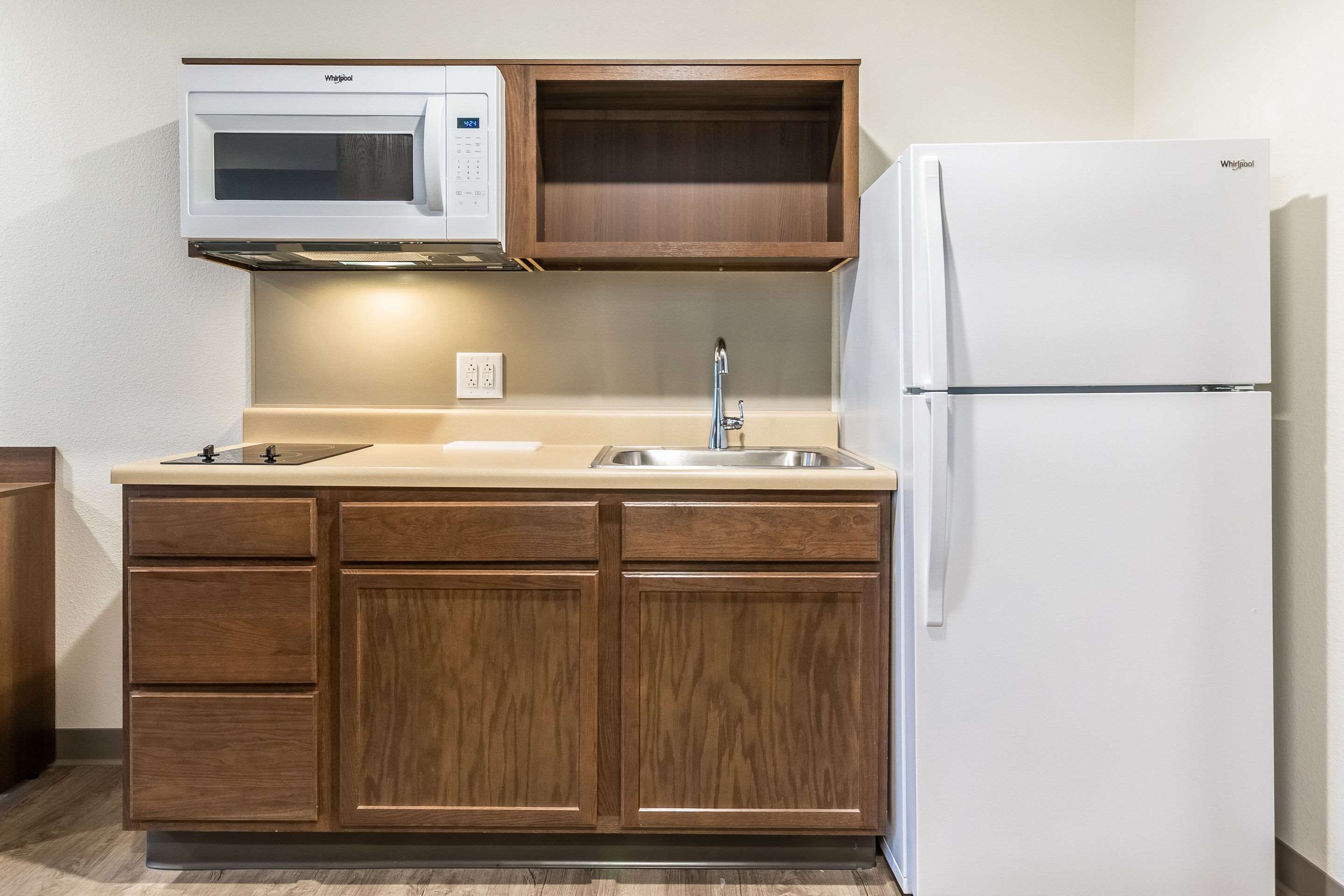 Una cocina compacta con armarios de madera, microondas integrado, pileta de acero inoxidable y refrigerador blanco.