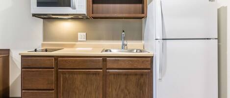 Una cocina compacta con armarios de madera, microondas integrado, pileta de acero inoxidable y refrigerador blanco.