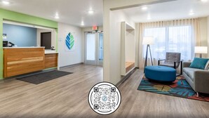 A hotel lobby with a reception desk, a waiting area with a sofa and armchair, and a large window with curtains. - WoodSpring Suites Indianapolis Castleton (Indianapolis)