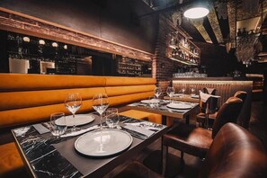 A restaurant with a brick wall, wooden bench seating, and a bar area with shelves of bottles. - Project 3 Urban Chic Hotel (Athens)