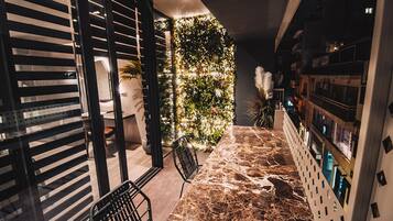 Un interior moderno con suelo de piedra, una zona de estar con sillas, una pared decorativa con plantas y una barra con estanterías.
