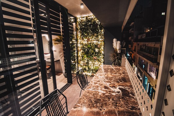 A modern interior with a stone floor, a seating area with chairs, a decorative wall with plants, and a bar area with shelves. - Project 3 Urban Chic Hotel (Athens)