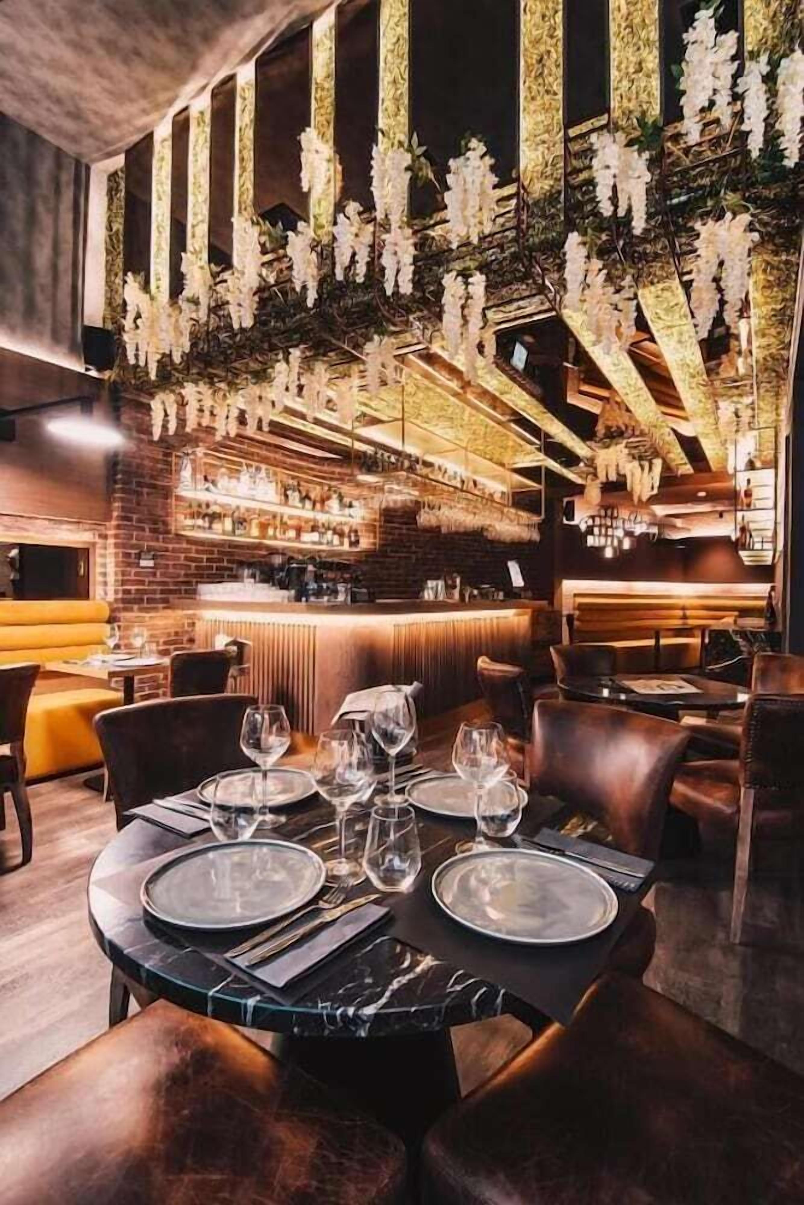 Un restaurante con zona de bar, asientos de cuero y un techo decorado con flores colgantes.