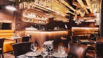 Un restaurante con zona de bar, asientos de cuero y un techo decorado con flores colgantes.