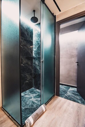 A modern bathroom with a glass shower enclosure, a marble-like wall, and a wooden floor. - Project 3 Urban Chic Hotel (Athens)