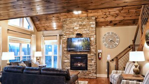 A living room with a stone fireplace, leather sofa, striped armchairs, and a large clock on the wall.